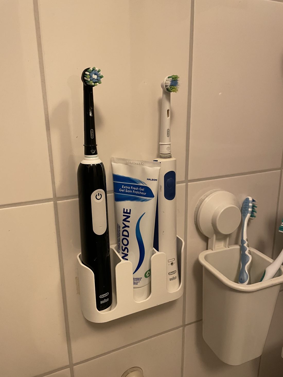 De houder gemonteerd aan de badkamerwand met twee elektrische tandenborstels en een tube tandpasta